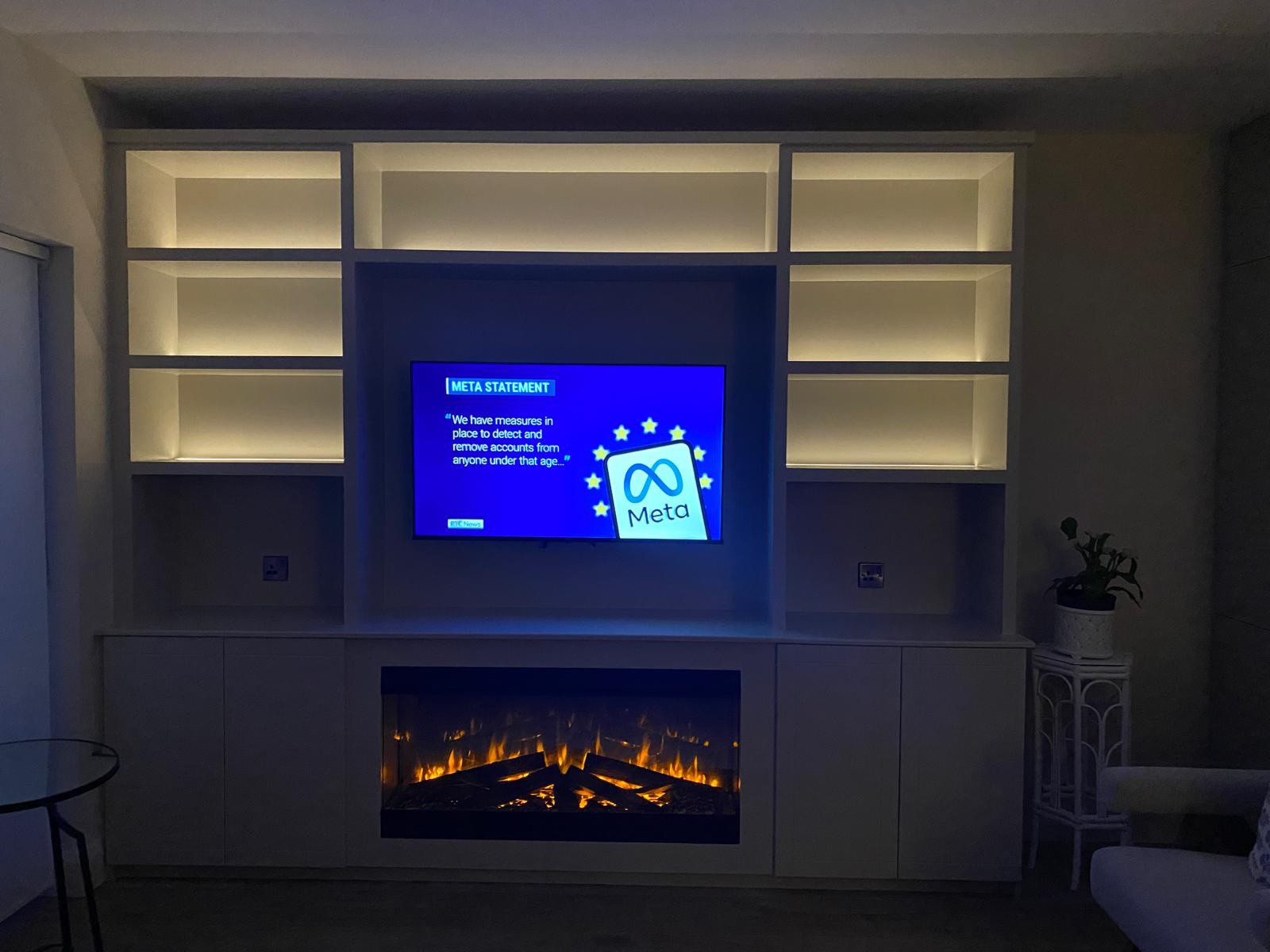Built-in media wall with LED-lit alcove shelves and electric fireplace